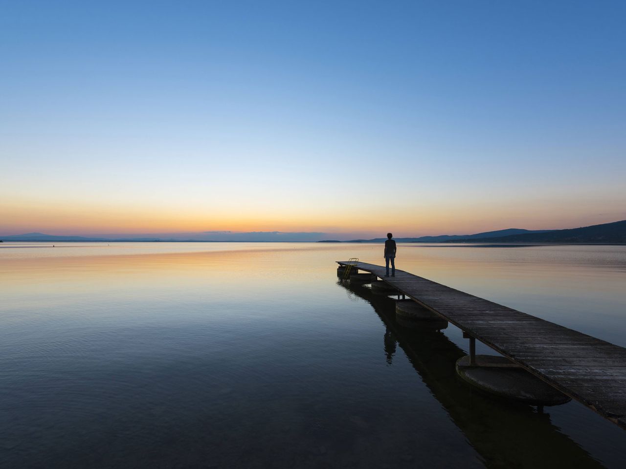 Person steht auf Steg im Lago di Trasimeno, Italien