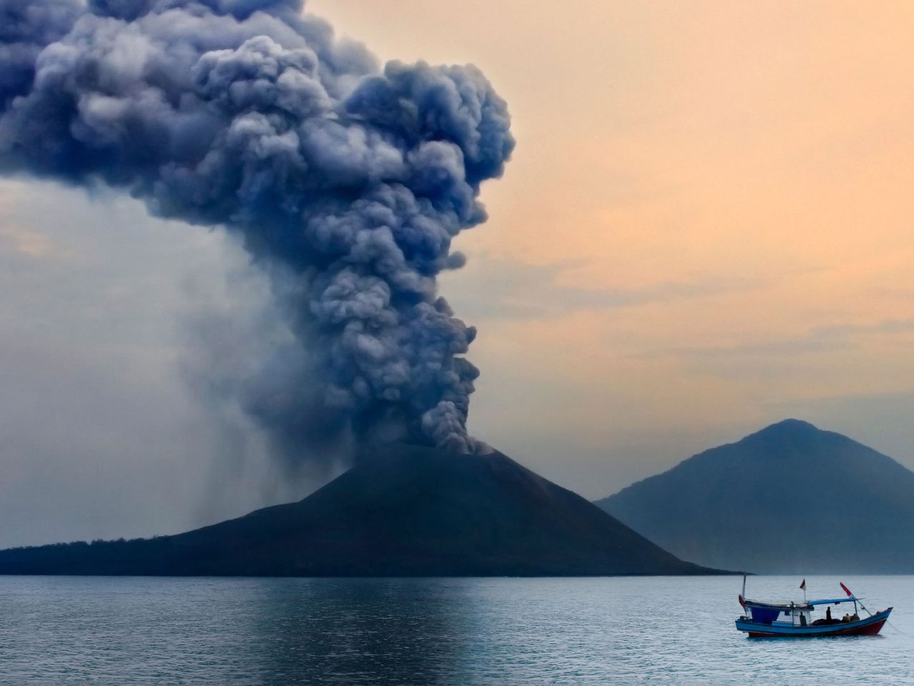 Ein Boot fährt am rauchenden Krakatau entlang.