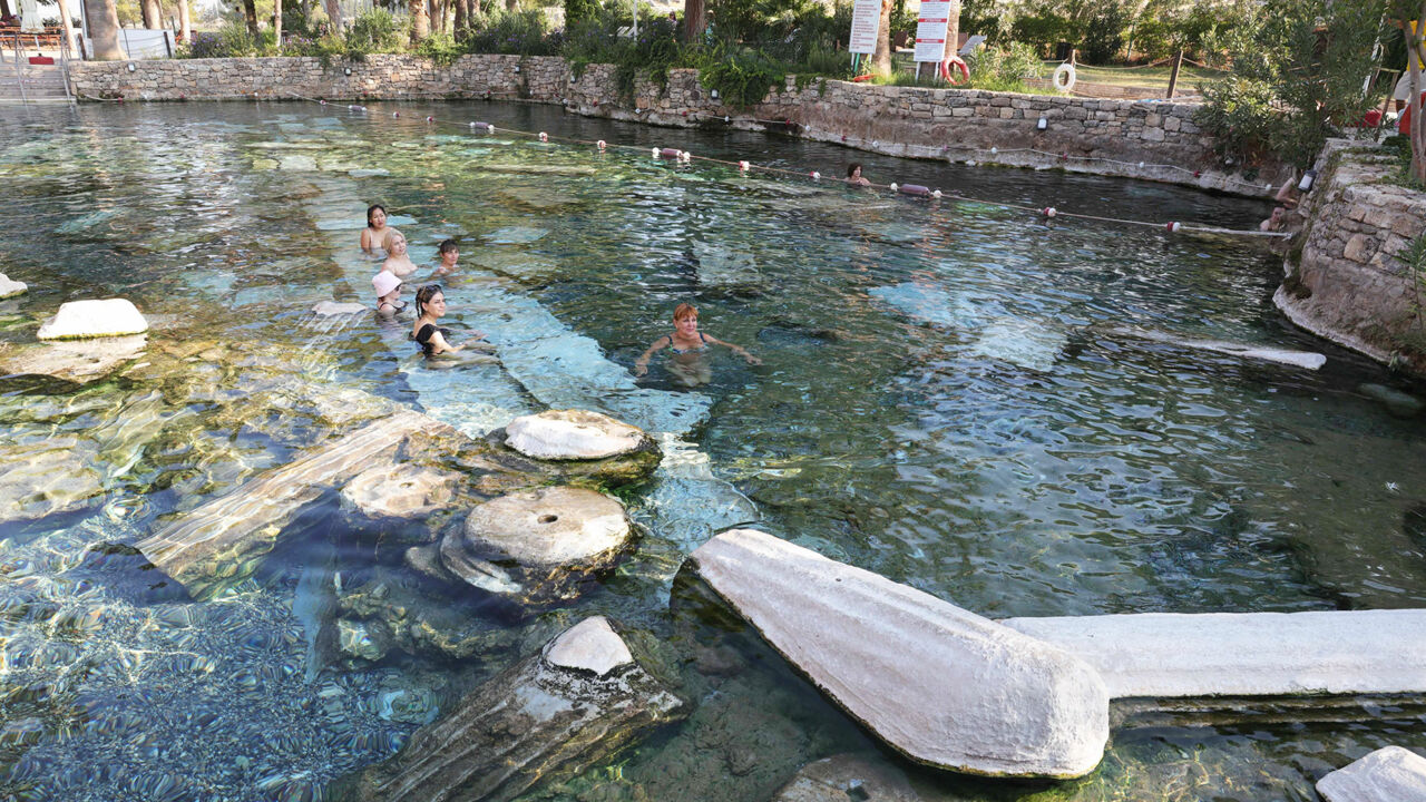 Badegäst:innen schwimmen zwischen antiken Säulen im Kleopatra Pool