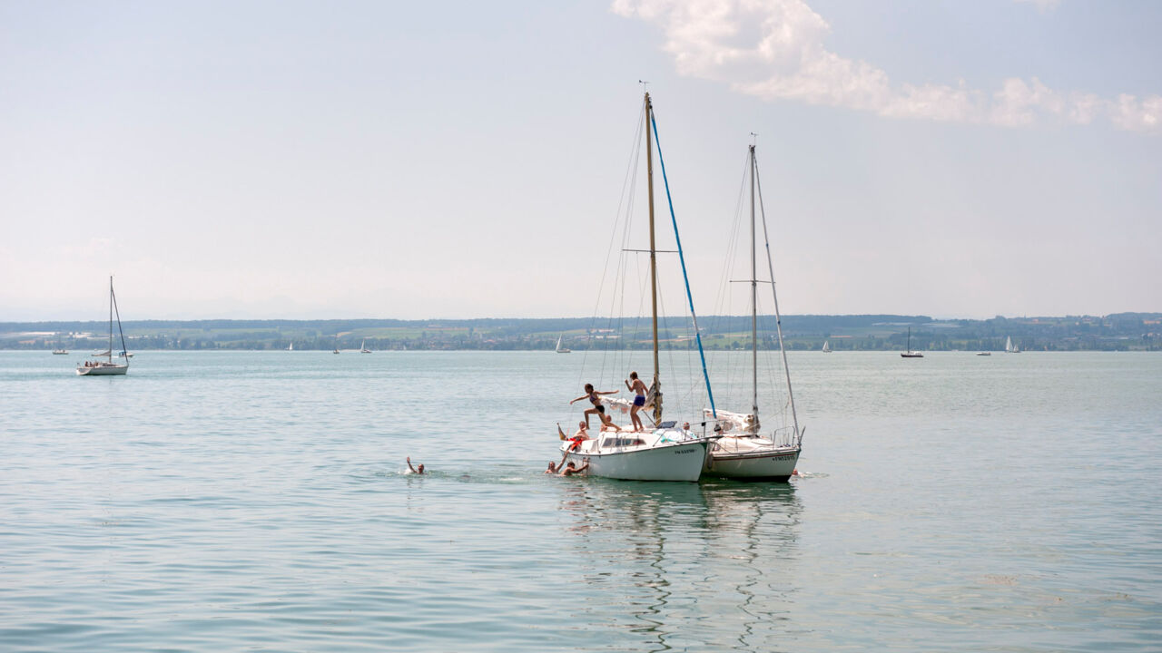 Kinder springen von Segelbooten ins Wasser des Bodensees