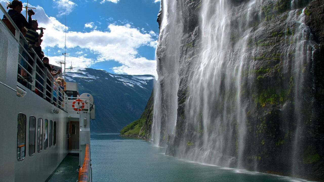 Passagiere beobachten den „Brautschleier“-Wasserfall im Geirangerfjord von Bord eines Schiffes. 