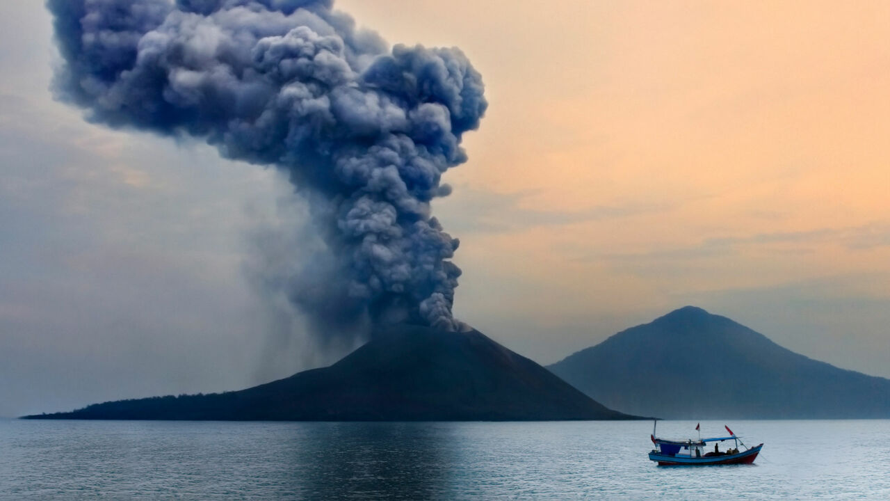 Ein Boot fährt am rauchenden Krakatau entlang.