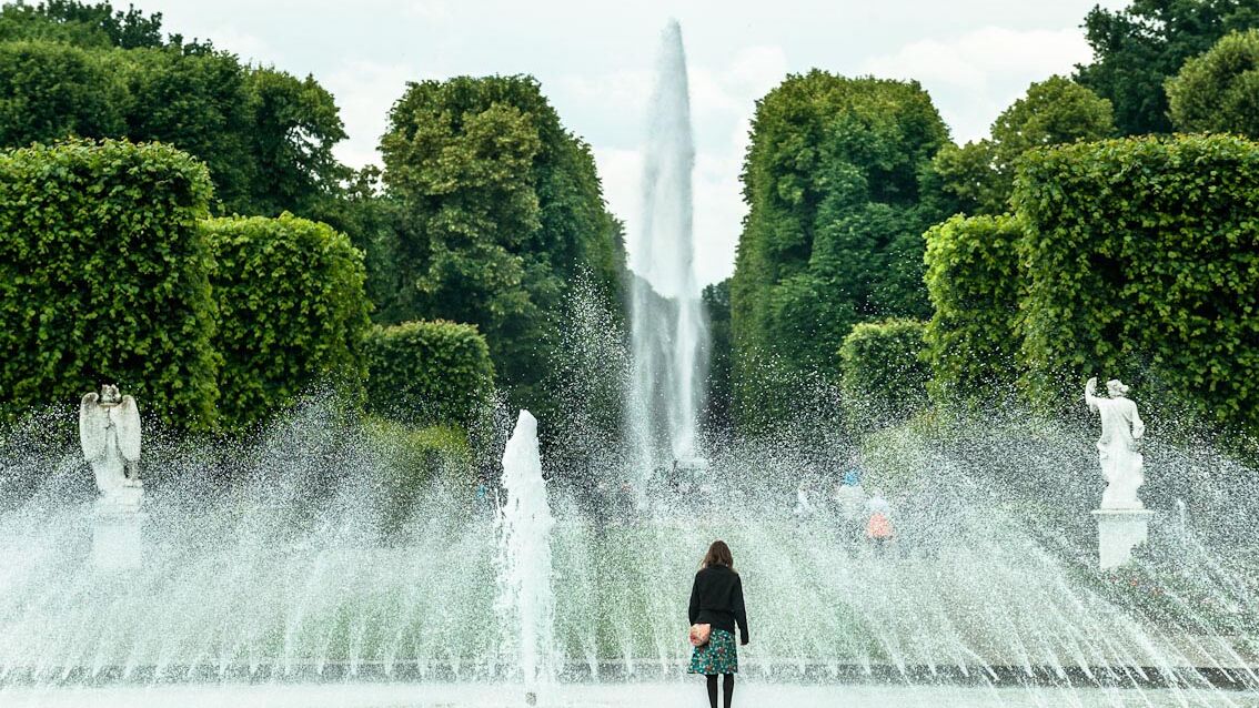 Eine Frau steht vor einer Fontäne im Großen Garten Hannover