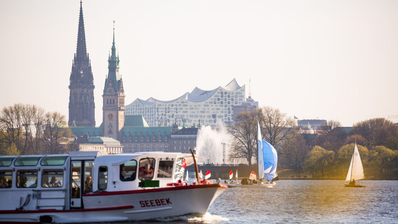 Blick auf die Außenalster in Hamburg mit Alsterdampfer, Elbphilharmonie, Segelboot, Rathaus, St. Nikolai.