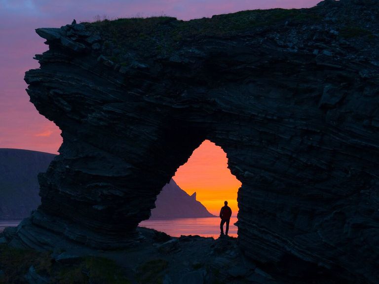 Person steht am Kirkeporten und blickt auf den Mefjorden, in der Dämmerung