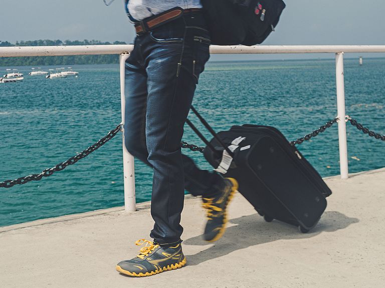 Das richtige Gepäck an Bord: Was nehme ich mit auf Kreuzfahrt? Ein Reisender geht mit Gepäck über einen Steg