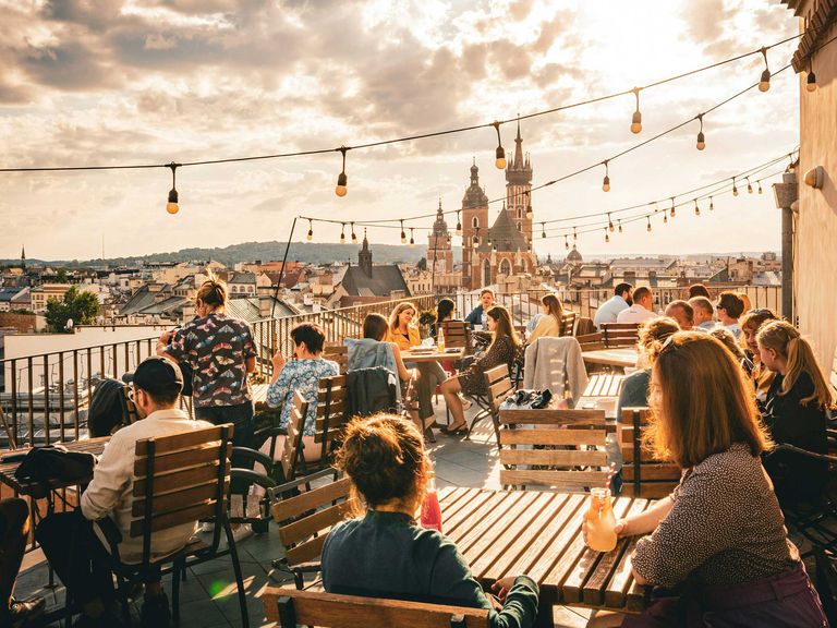 Krakau und andere polnische Städte boomen derzeit – und versprechen dennoch Entspannung. Menschen sitzen auf einer Dachterrasse in Krakau