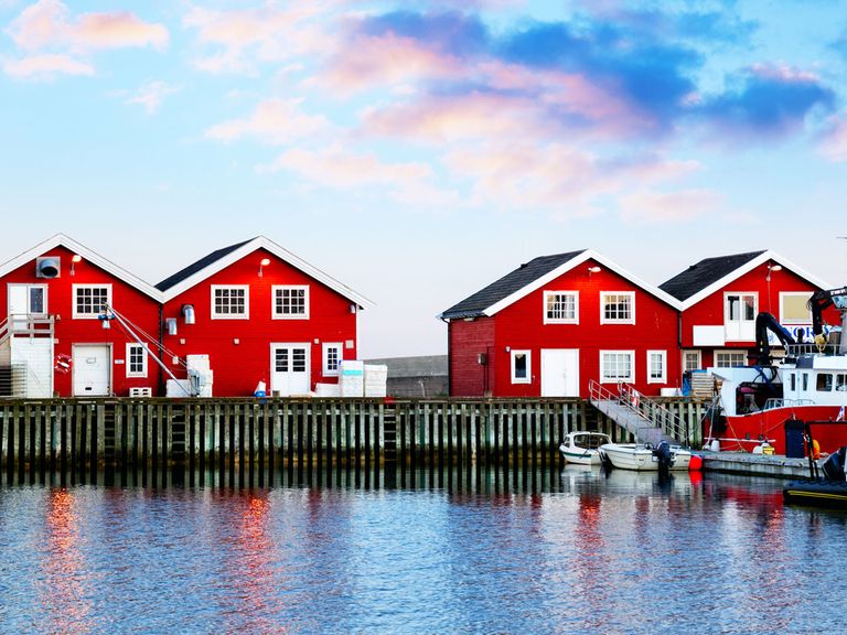 rote Holzhäuser und ein Boot am Hafen von Bodø 