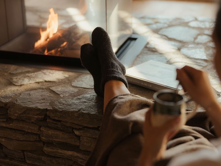 Kann sein, dass in der Eriro-Suite ein Paar Wollsocken bereitliegt. Hilft beim Runterkommen. Frau trinkt Tee vorm Kamin im eriro Alpine hide