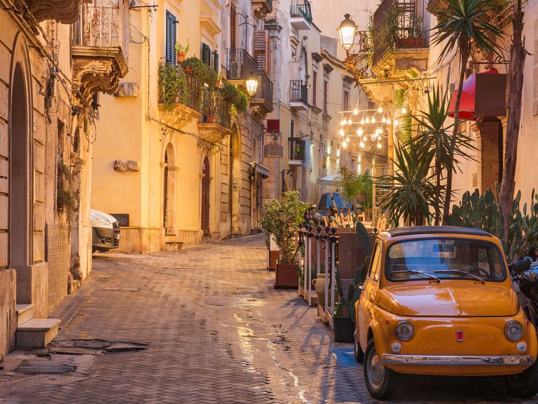 Sizilien blüht im Mai richtig auf, Städte wie Syrakus sind ganzjährig ein Hingucker. Gelbes Auto in einer Gasse von Syrakus