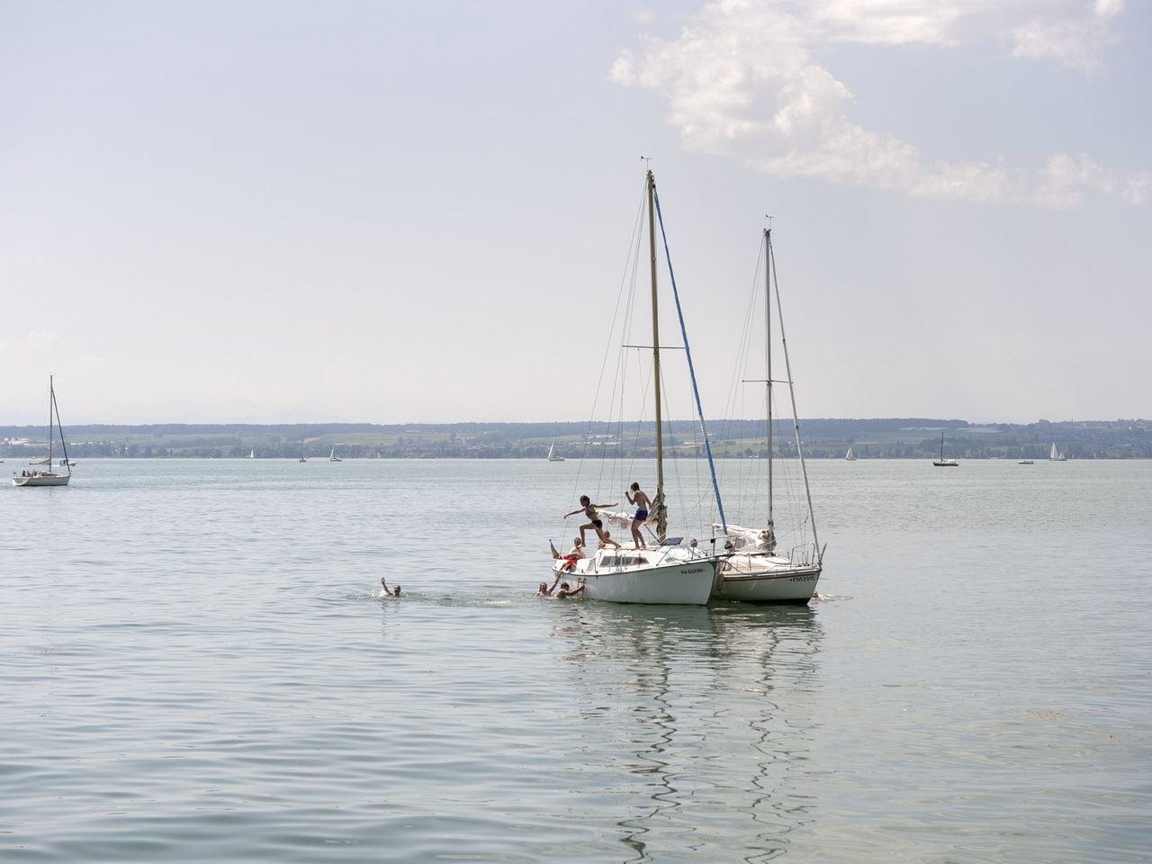 Kinder springen von Segelbooten ins Wasser des Bodensees