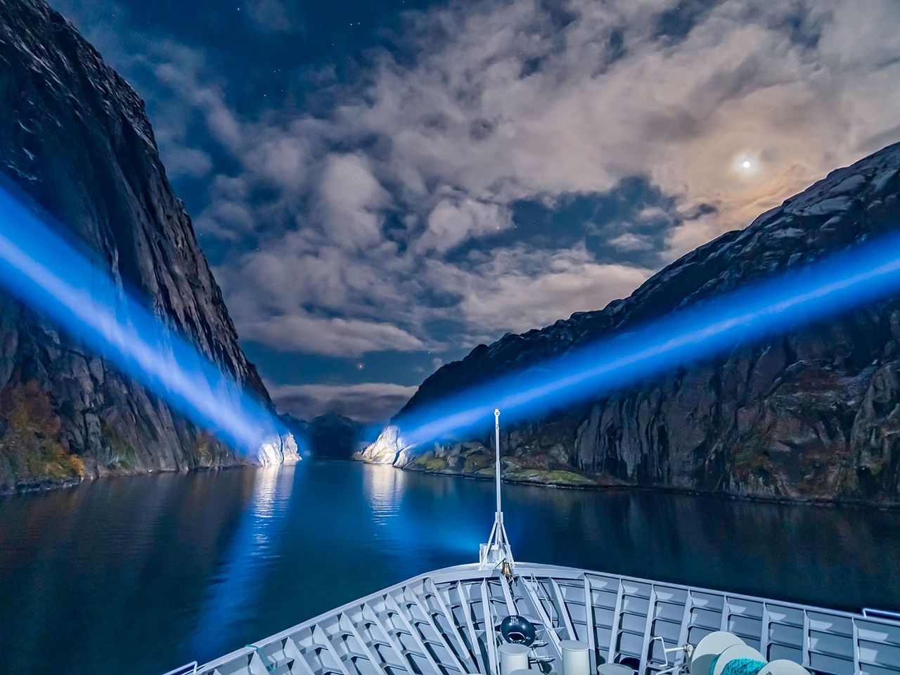 Ein Kreuzfahrtschiff beleuchtet nachts mit Scheinwerfern die Felswände des Trollfjords. 