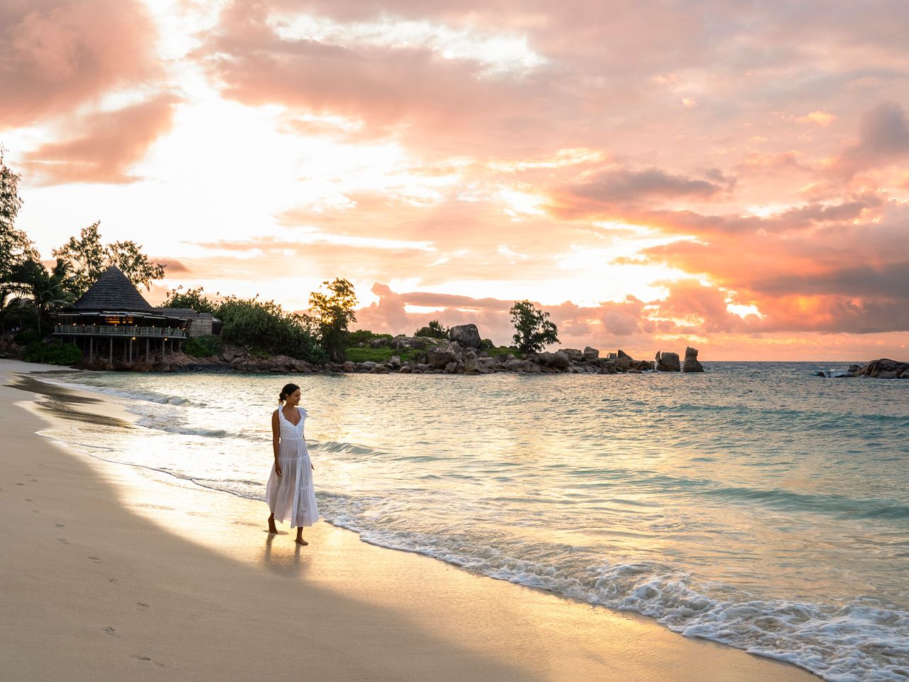 Frau spaziert am Anse Kerlan, im Hintergrund Restaurant The Nest