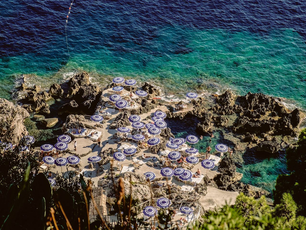 Sonnenschirme und -liegen auf zerklüfteten Felsen, La Fontelina Capri