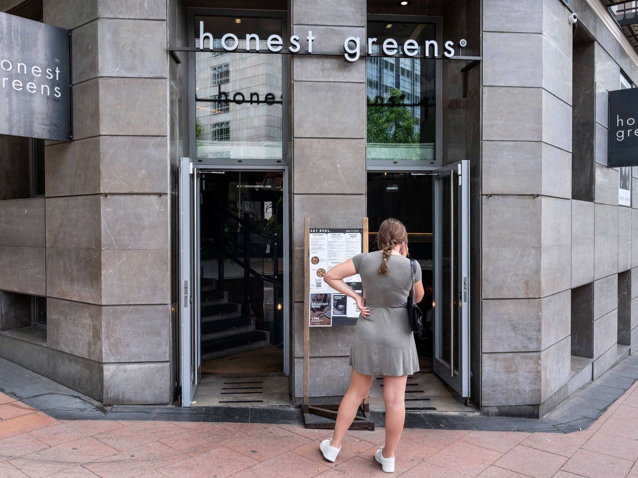 Frau steht vor einer Filiale von Honest Greens in Madrid