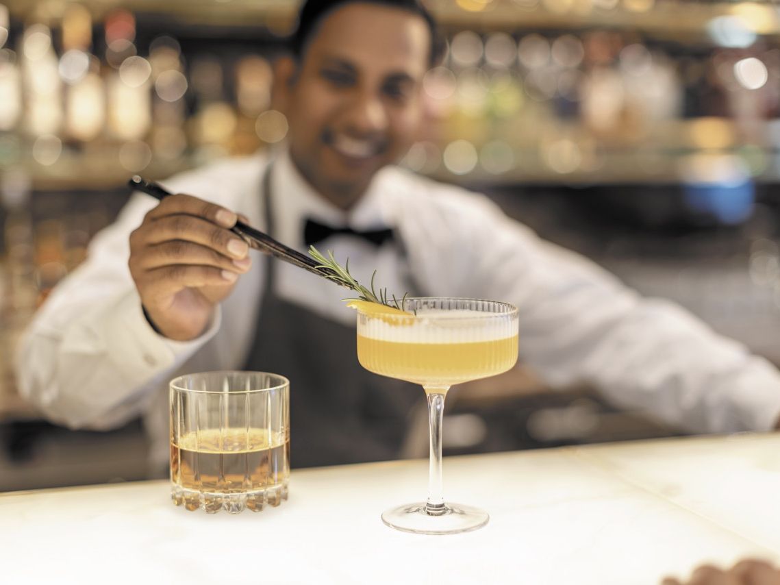 Ein Barkeeper garniert einen Cocktail an einer eleganten Bar auf einem Regent-Schiff.