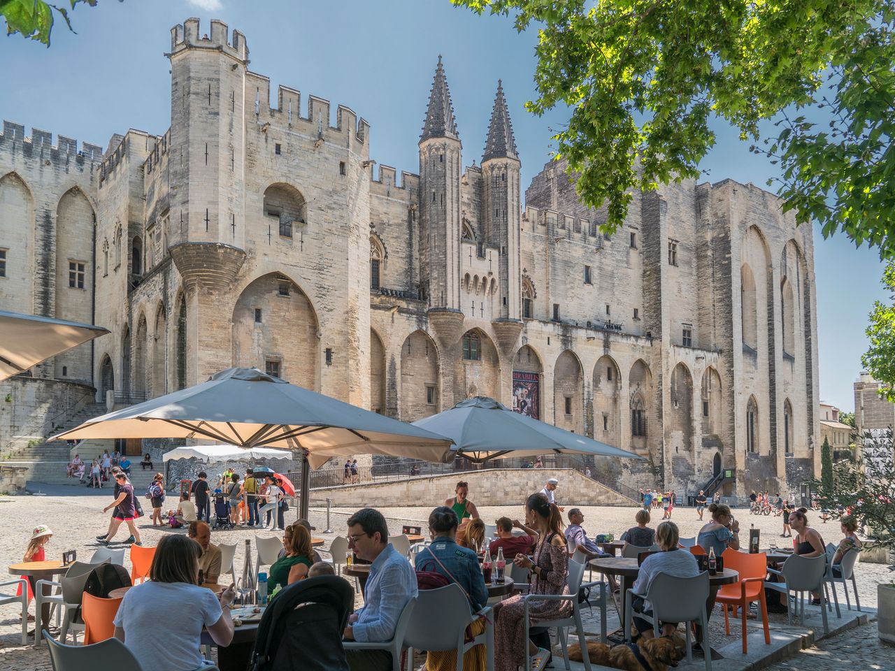 Menschen sitzen vor dem Papstpalast in der Altstadt von Avignon