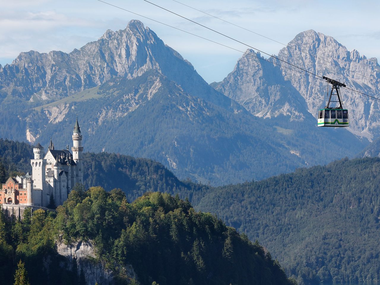 Panorama auf Schloss Neuschwanstein im Allgäu in Bayern mit Blick auf eine Gondel der Tegelberg Kabinenbahn in den Ammergauer Alpen
