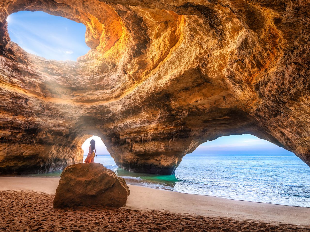 Frau steht auf einem kleinen Felsen in der Benagil-Höhle, Algarve