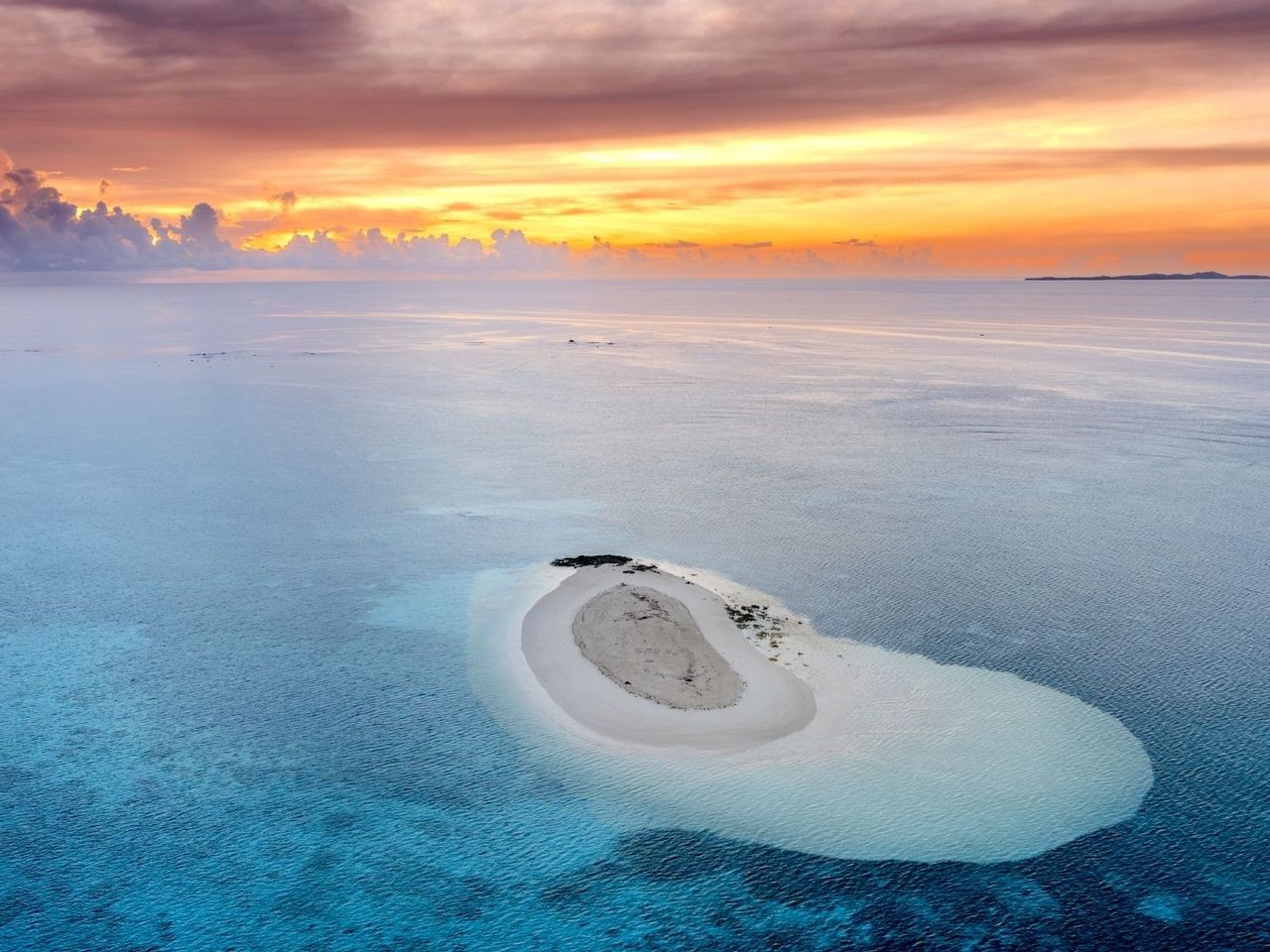 Eine leere Sandinsel mitten im türkisfarbenen Ozean bei Sonnenaufgang