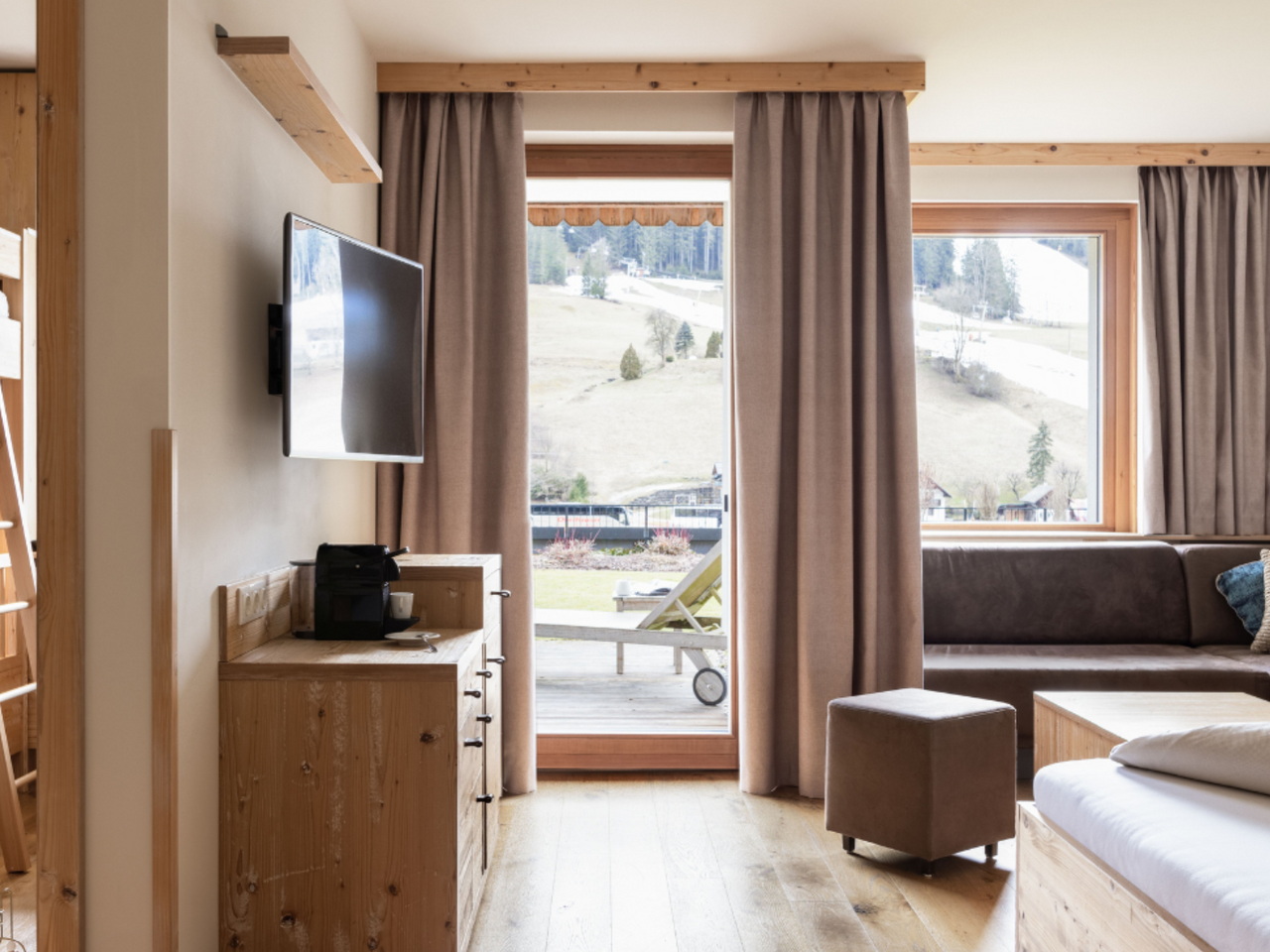 Helles Chalet mit Holzboden, Etagenbett, Sitzecke, Fernseher und großen Fenstern mit Blick auf die Landschaft.