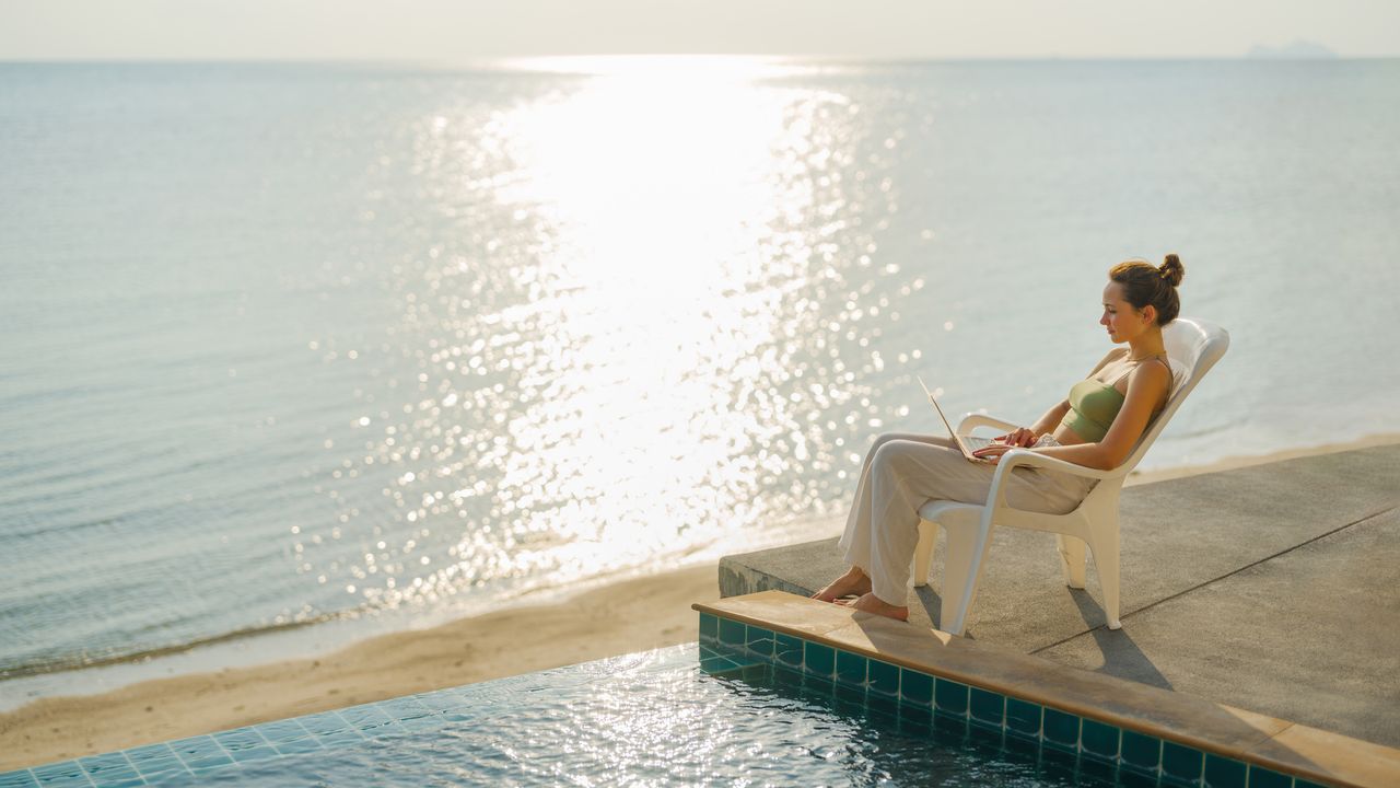 Workation, Frau sitzt mit Laptop am Pool