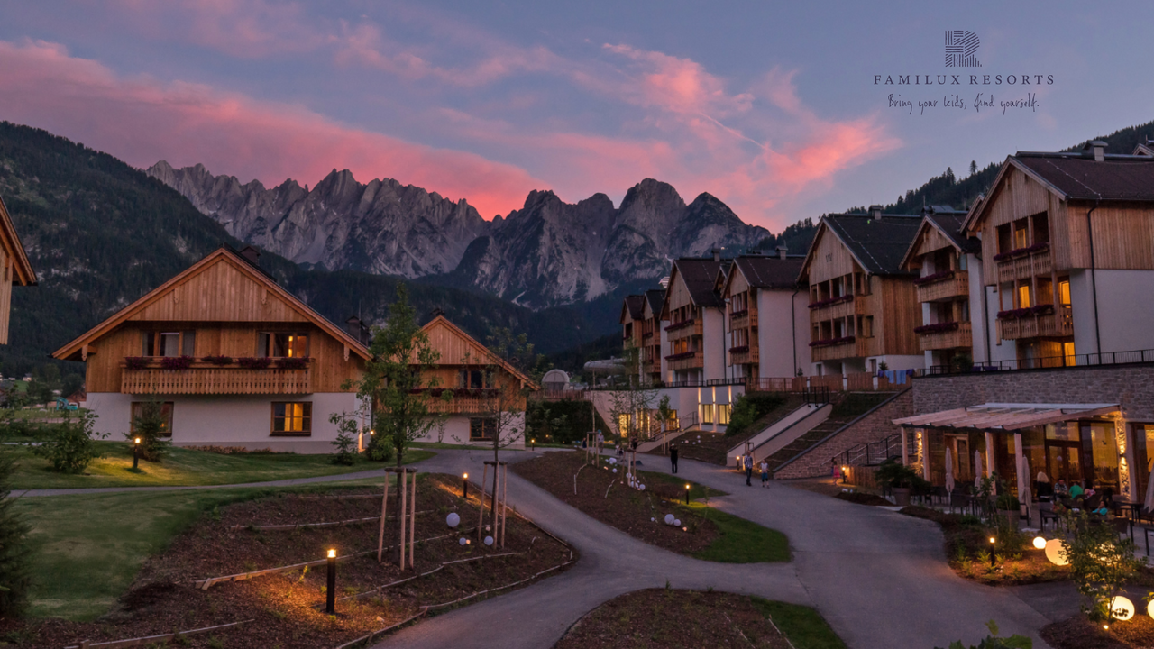Chaletdorf vor imposanter Bergkulisse im Abendlicht.