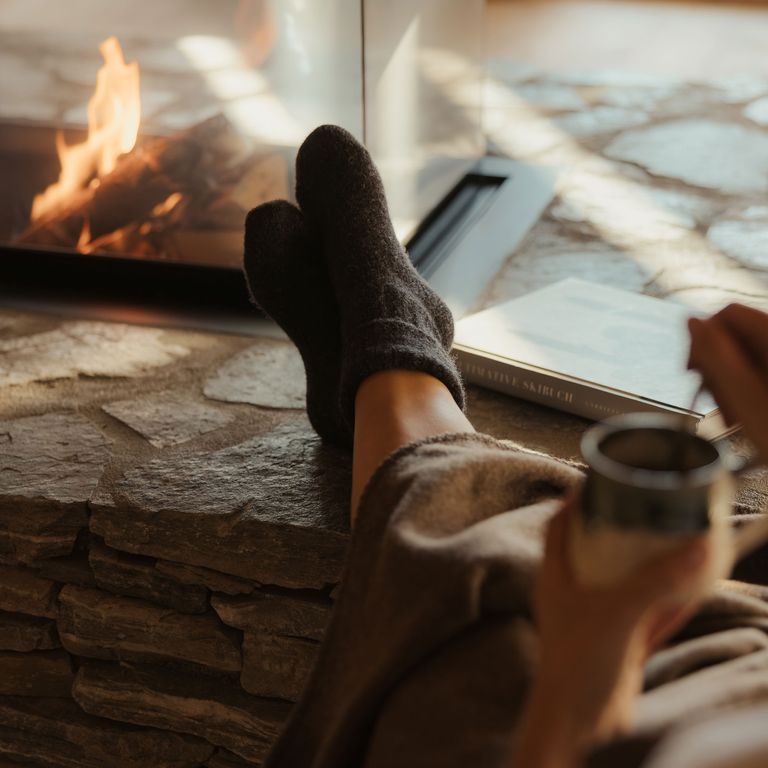Kann sein, dass in der Eriro-Suite ein Paar Wollsocken bereitliegt. Hilft beim Runterkommen. Frau trinkt Tee vorm Kamin im eriro Alpine hide